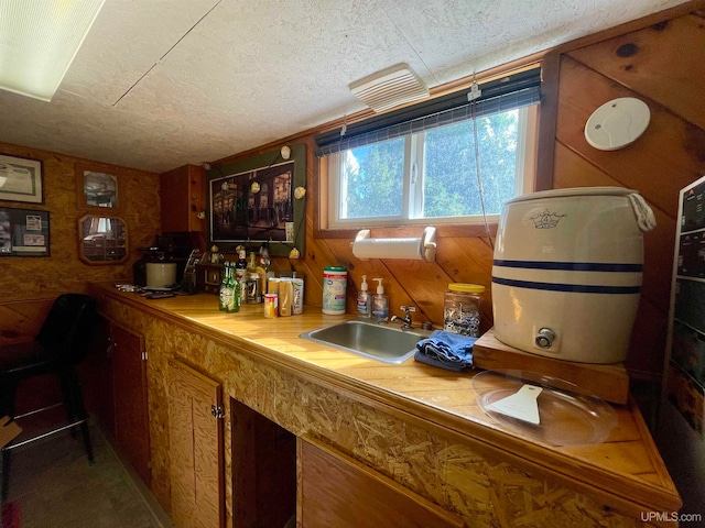 bar featuring a textured ceiling, wood walls, and sink