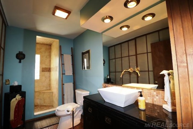 bathroom with a tile shower, vanity, and toilet