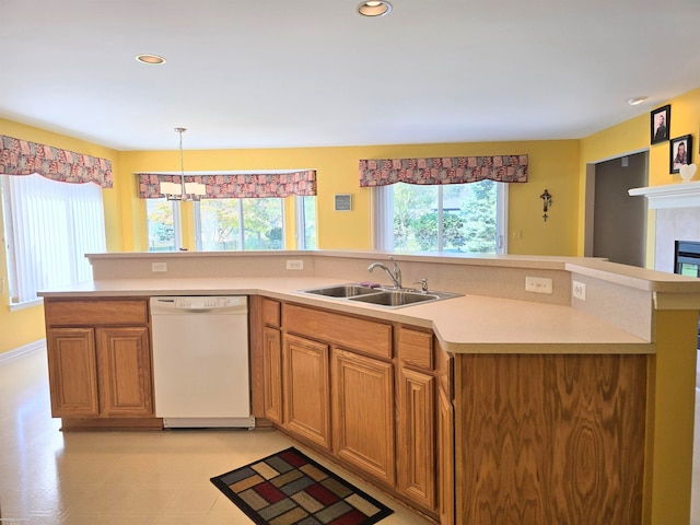 kitchen featuring a tile fireplace, pendant lighting, white dishwasher, sink, and a notable chandelier