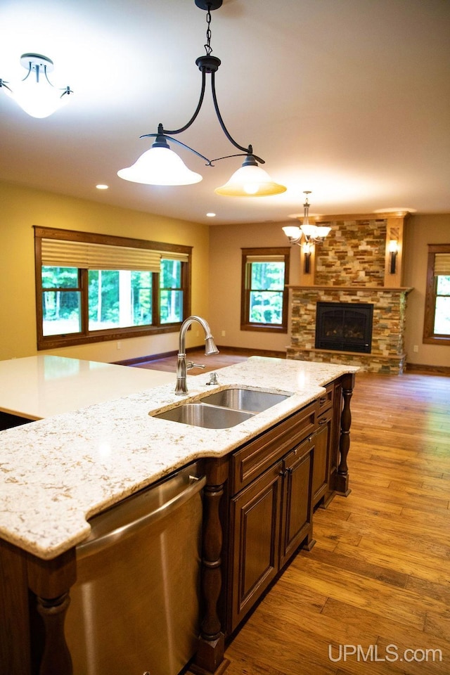 kitchen featuring light hardwood / wood-style floors, sink, a fireplace, decorative light fixtures, and stainless steel dishwasher