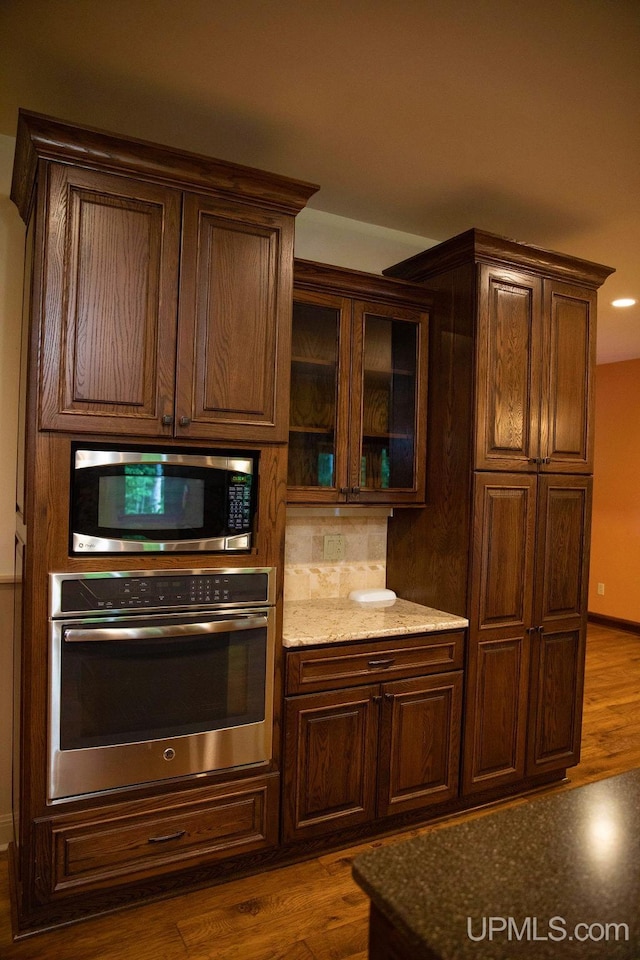 kitchen featuring stainless steel appliances, light stone counters, dark wood-type flooring, and tasteful backsplash