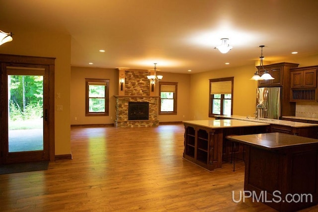 kitchen featuring a stone fireplace, decorative light fixtures, light hardwood / wood-style flooring, and stainless steel fridge with ice dispenser