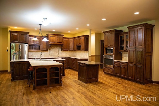 kitchen with dark brown cabinetry, an island with sink, decorative light fixtures, stainless steel appliances, and light hardwood / wood-style floors