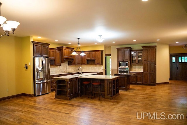 kitchen with wood-type flooring, decorative light fixtures, an island with sink, and appliances with stainless steel finishes