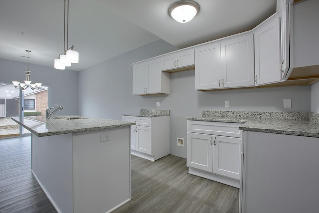 kitchen featuring white cabinets, a kitchen island with sink, decorative light fixtures, a notable chandelier, and light wood-type flooring