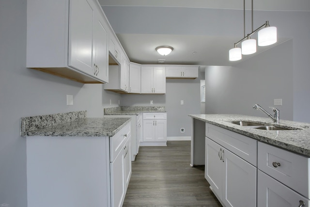 kitchen with hanging light fixtures, sink, white cabinetry, dark hardwood / wood-style floors, and light stone countertops