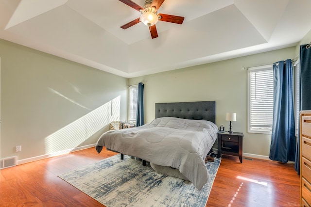 bedroom featuring light wood-type flooring, a tray ceiling, and ceiling fan