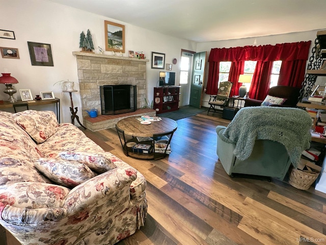 living room featuring a baseboard radiator, dark wood-type flooring, and a stone fireplace