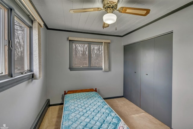 carpeted bedroom with ceiling fan, a closet, crown molding, and a baseboard heating unit