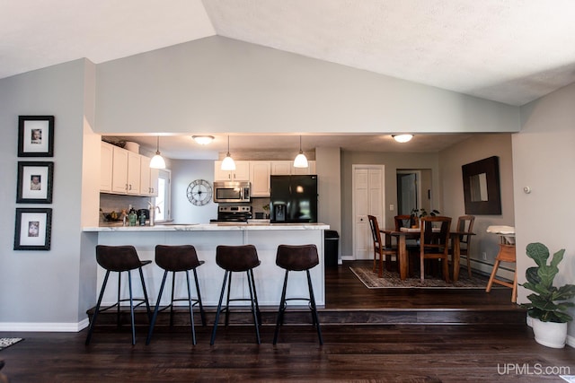 kitchen featuring stainless steel appliances, white cabinets, kitchen peninsula, and vaulted ceiling