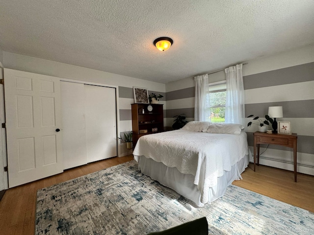 bedroom with hardwood / wood-style flooring, baseboard heating, and a textured ceiling