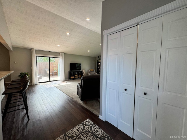 hall with a textured ceiling, vaulted ceiling, and dark hardwood / wood-style floors