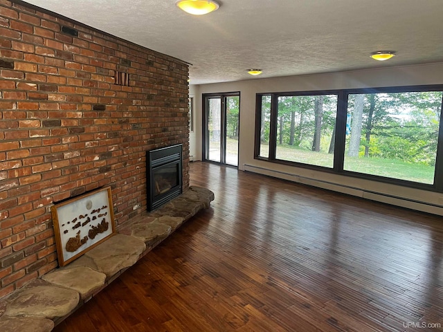 unfurnished living room featuring a baseboard heating unit, a textured ceiling, dark wood-type flooring, a fireplace, and brick wall