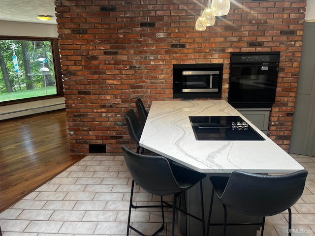 kitchen featuring light hardwood / wood-style flooring, black appliances, baseboard heating, and a kitchen breakfast bar