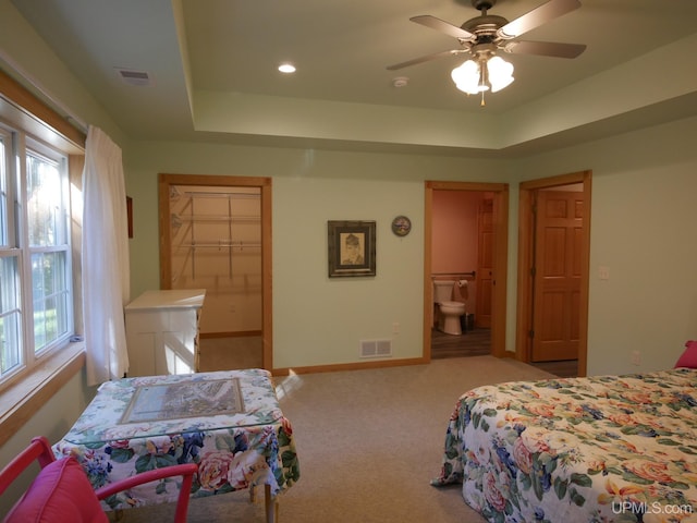 carpeted bedroom with multiple windows, a raised ceiling, ensuite bathroom, and ceiling fan