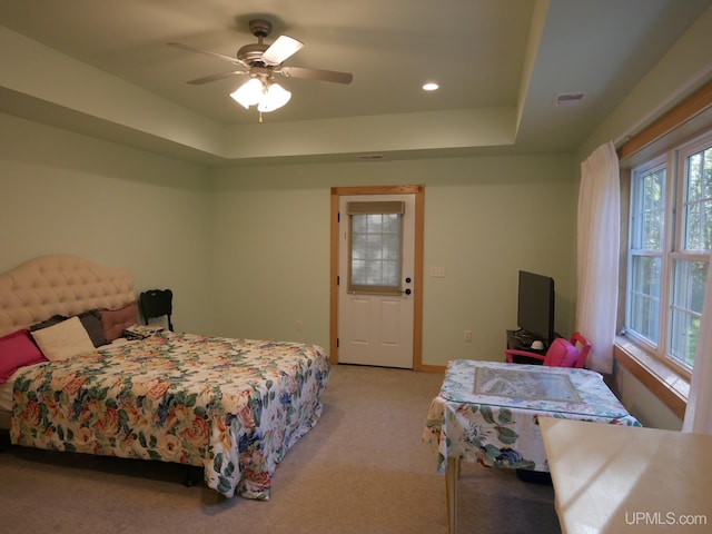 bedroom with ceiling fan, a tray ceiling, and light carpet