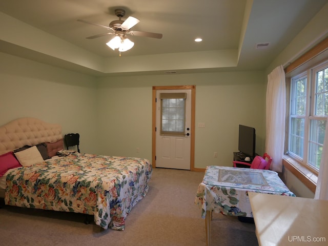 bedroom with light carpet, baseboards, a tray ceiling, and a ceiling fan