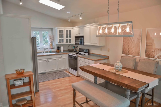 kitchen with hanging light fixtures, white cabinets, gas range gas stove, lofted ceiling, and light hardwood / wood-style flooring