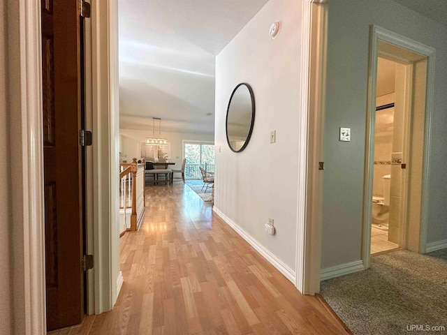 corridor with light wood-type flooring and a notable chandelier