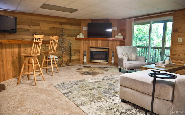 carpeted living room with wood walls and a drop ceiling