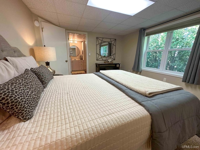 bedroom featuring ensuite bath and a drop ceiling