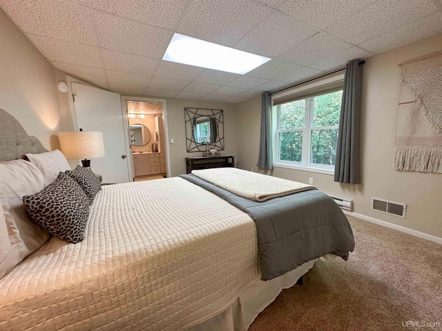 carpeted bedroom with connected bathroom, a baseboard radiator, and a drop ceiling