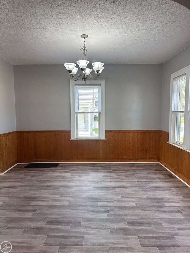 empty room featuring a textured ceiling, light wood-type flooring, wooden walls, and a notable chandelier