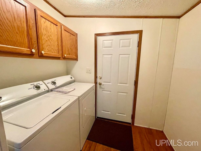 laundry area featuring washing machine and dryer, dark hardwood / wood-style flooring, a textured ceiling, crown molding, and cabinets