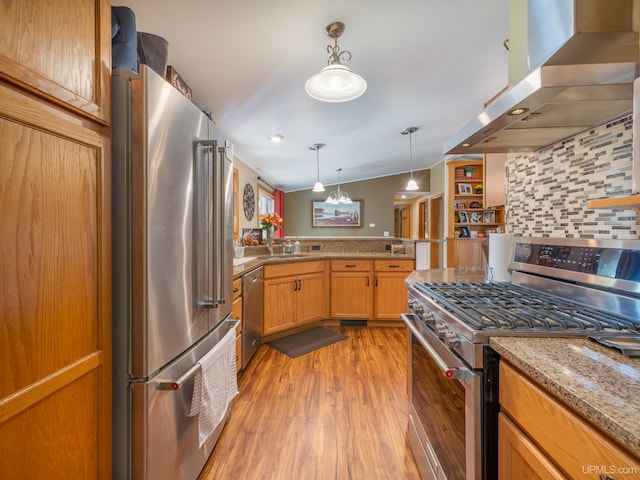 kitchen with light hardwood / wood-style floors, vaulted ceiling, hanging light fixtures, premium appliances, and wall chimney exhaust hood