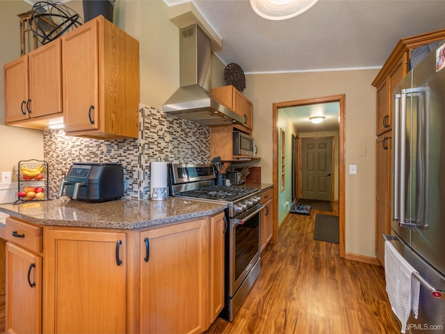 kitchen featuring wall chimney range hood, decorative backsplash, appliances with stainless steel finishes, dark hardwood / wood-style flooring, and ornamental molding