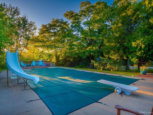 view of pool with a water slide, a patio area, and a diving board