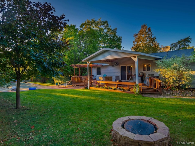 back of property with a lawn, a deck, and an outdoor fire pit