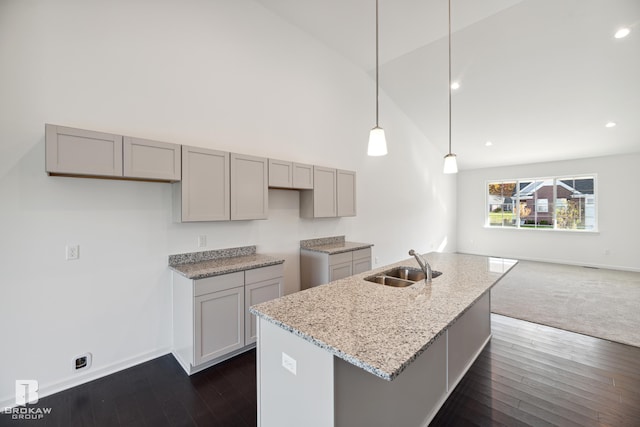 kitchen with a center island with sink, sink, light stone counters, gray cabinets, and pendant lighting