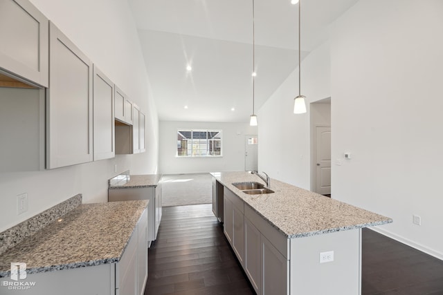 kitchen featuring dark wood-type flooring, light stone counters, sink, a kitchen island with sink, and pendant lighting