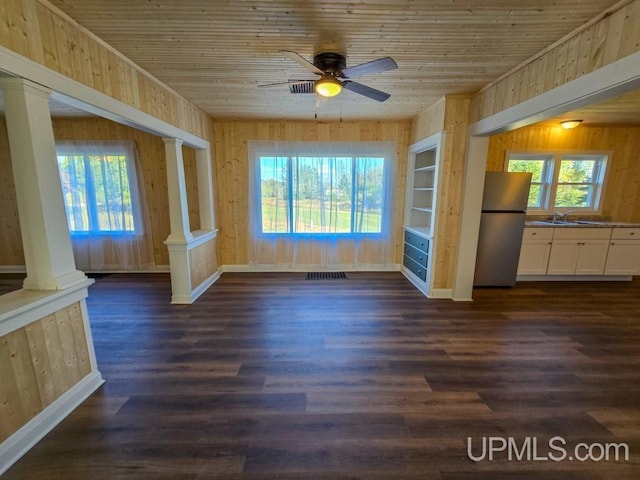 interior space featuring built in features, wooden walls, dark hardwood / wood-style flooring, ceiling fan, and ornate columns