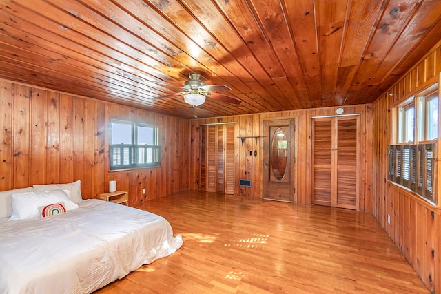 bedroom featuring wooden walls, wooden ceiling, multiple closets, and light wood-type flooring