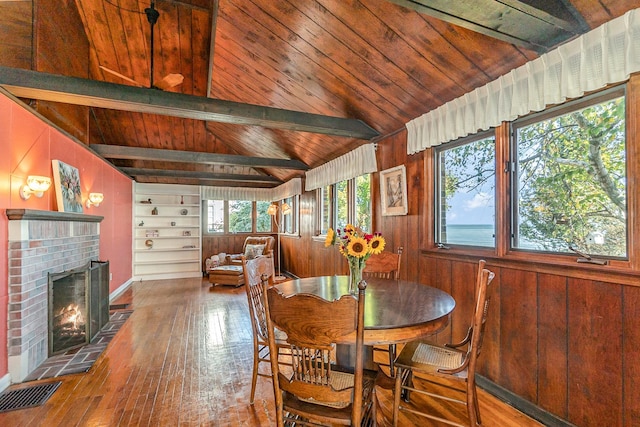 dining room featuring wood ceiling, hardwood / wood-style floors, a fireplace, lofted ceiling with beams, and wood walls