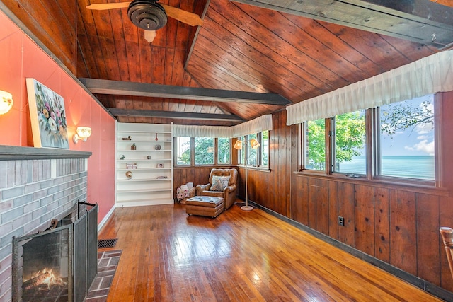 unfurnished room with lofted ceiling with beams, wood ceiling, a fireplace, and wood walls