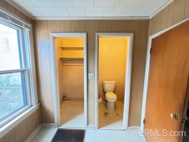 bathroom with toilet, crown molding, and wood walls