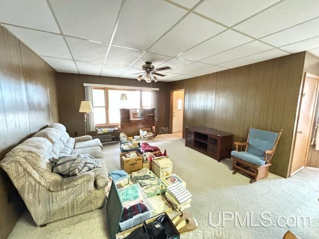 living room with a paneled ceiling, wooden walls, ceiling fan, and carpet