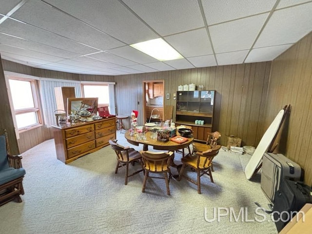 dining room featuring a drop ceiling, carpet floors, and wooden walls