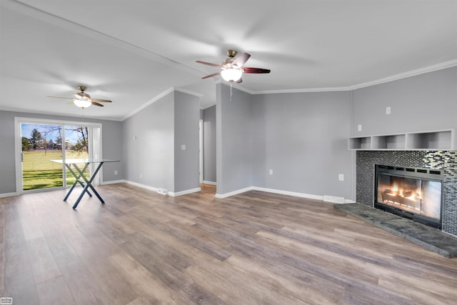 unfurnished living room featuring wood-type flooring, ceiling fan, a tile fireplace, and crown molding