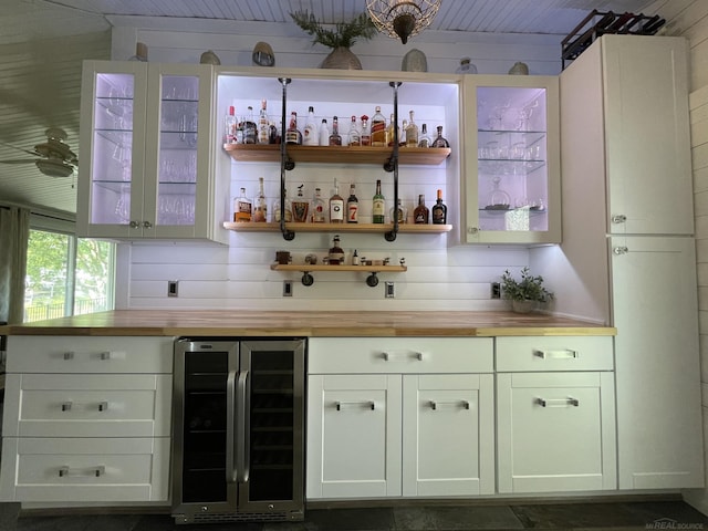 bar with wine cooler, wooden counters, and white cabinetry