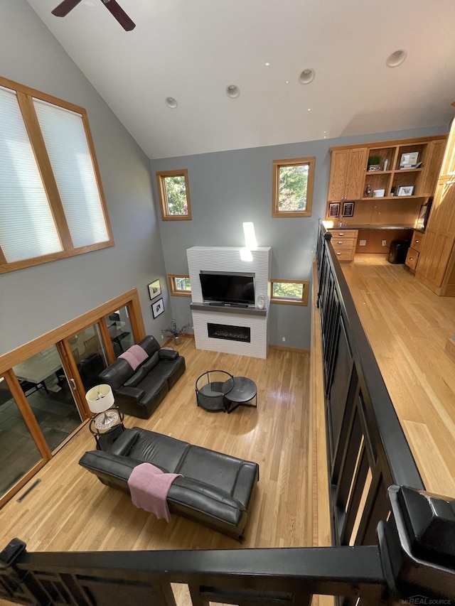 living room featuring light wood-type flooring, vaulted ceiling, ceiling fan, and a large fireplace