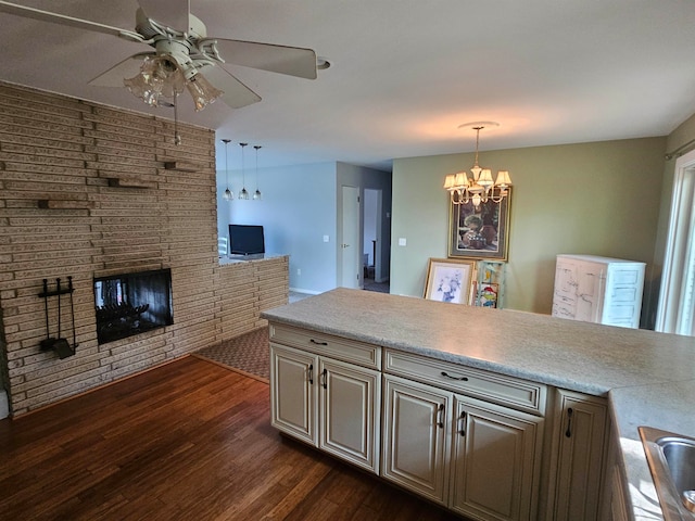 kitchen featuring hanging light fixtures, a fireplace, ceiling fan with notable chandelier, and dark wood-type flooring