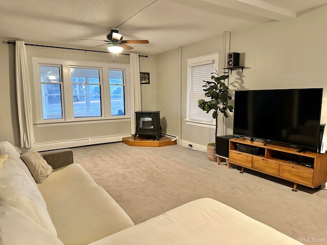 carpeted living room with a baseboard heating unit, a wood stove, a wealth of natural light, and ceiling fan