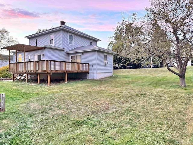 back house at dusk with a lawn and a deck