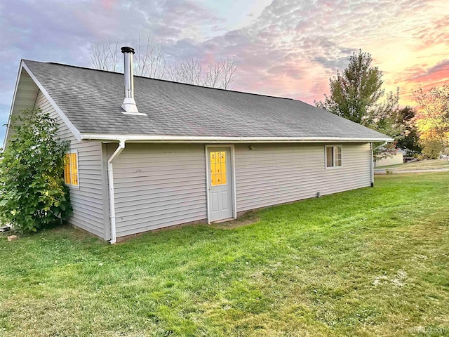 back house at dusk featuring a lawn