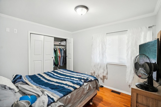 bedroom with wood-type flooring, crown molding, and a closet