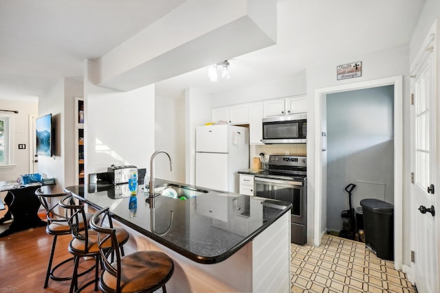 kitchen with stainless steel appliances, white cabinets, a kitchen bar, and sink